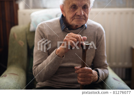 Sad elderly man with walking stick sitting on armchair indoors at home, resting. 81276077