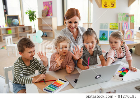 Group of small nursery school children with teacher indoors in classroom, using laptop. 81276183