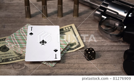 A dangerous game for money. On a wooden table are a pistol with cartridges, cash dollars, a deck of playing cards with an ACE of spades and a dice. Dangerous gambling debts and loans. A dangerous game for money. On a wooden table are a pistol with cartridges, cash dollars, a deck of playing cards with an ACE of spades and a dice. Dangerous gambling debts and loans. 81276909