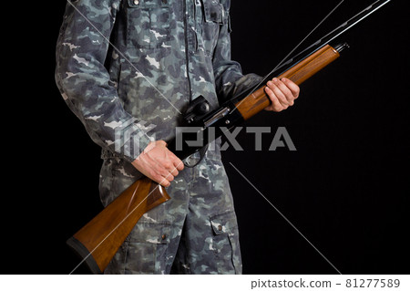 Soldier or hunter on a black background, isolated, copy space. Young man with a gun. A soldier in military uniform with a shotgun. War games. Preparation for spring, autumn hunting. 81277589