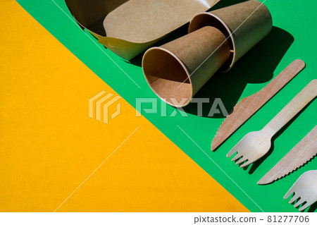 Wooden forks and paper cups with plates on color background. Eco friendly disposable tableware. Used in fast food, restaurants, takeaways, picnics. No plastic 81277706