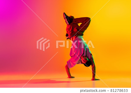 Portrait of young stylish man, break dancing dancer training in casual clothes isolated over gradient pink yellow background at dance hall in neon light. 81278633