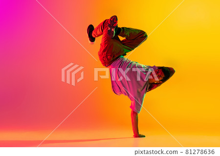 In action. Young man, break dancing dancer ptacticing in casual clothes isolated over gradient pink yellow background at dance hall in neon light. In action. Young man, break dancing dancer ptacticing in casual clothes isolated over gradient pink yellow background at dance hall in neon light. 81278636