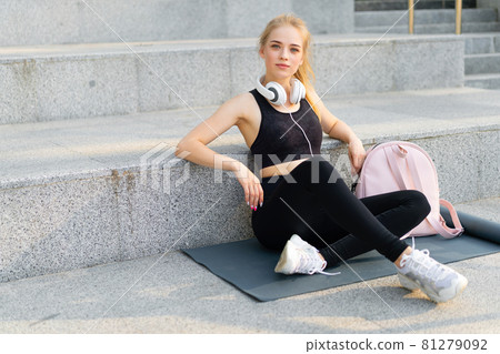Sport and Fitness Young Adult Caucasian Woman Sitting Exercise Mat Concrete Floor Resting after morning Workout Outdoor Summer Park 81279092