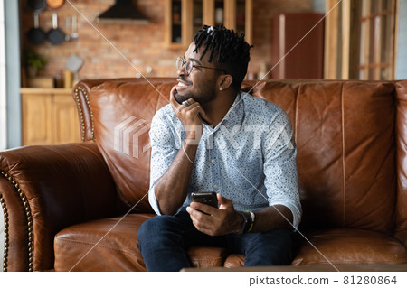 Thoughtful millennial African guy with mobile phone looking at window Thoughtful millennial African guy with mobile phone looking at window 81280864