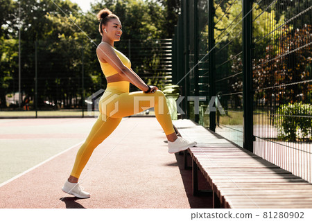 Smiling Black Woman In Yellow Sportswear Stretching Leg Outdoors Smiling Black Woman In Yellow Sportswear Stretching Leg Outdoors 81280902