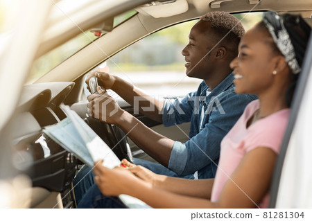 Cheerful black lady helping her driving boyfriend, checking map Cheerful black lady helping her driving boyfriend, checking map 81281304