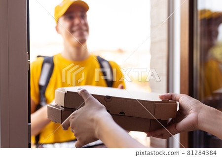 Young deliveryman in yellow uniform delivers order to clients, customers, buyers. Work, career, different professions concept. Idea of convenience, speed, comfort, safety, service. 81284384