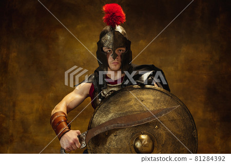 Close up of medieval person, brutal man, warrior or knight in war equipment isolated on vintage dark background. Comparison of eras, art, history, retro style concept Close up of medieval person, brutal man, warrior or knight in war equipment isolated on vintage dark background. Comparison of eras, art, history, retro style concept 81284392