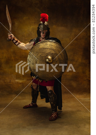 Full length portrait of medieval person, brutal man, warrior or knight in war equipment isolated on vintage dark background. Comparison of eras, art, history, retro style concept Full length portrait of medieval person, brutal man, warrior or knight in war equipment isolated on vintage dark background. Comparison of eras, art, history, retro style concept 81284394