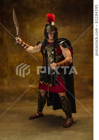 Portrait of medieval person, brutal man, warrior or knight in war equipment isolated on vintage dark background. Comparison of eras, art, history, retro style concept Portrait of medieval person, brutal man, warrior or knight in war equipment isolated on vintage dark background. Comparison of eras, art, history, retro style concept 81284395
