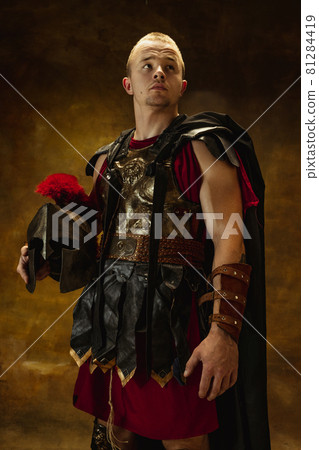 Full length portrait of medieval person, brutal man, warrior or knight in war equipment isolated on vintage dark background. Comparison of eras, art, history, retro style concept Full length portrait of medieval person, brutal man, warrior or knight in war equipment isolated on vintage dark background. Comparison of eras, art, history, retro style concept 81284419