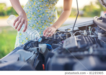 Fixing Her Broken Down Car, a young woman pours a water for washing glasses into her car. Fixing Her Broken Down Car, a young woman pours a water for washing glasses into her car. 81285905