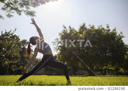 Morning sun flare with lady fitness trainer stretching showing strong abs and arms outdoors.  81286198