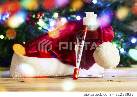 Covid-19 and Christmas holidays. Antiseptic hand sanitizer bottle, syringe and medicines on wood. Santa cap, coronavirus vaccines and syringe over Xmas tree Covid-19 and Christmas holidays. Antiseptic hand sanitizer bottle, syringe and medicines on wood. Santa cap, coronavirus vaccines and syringe over Xmas tree 81288922