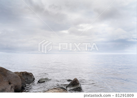 Beautiful autumn misty grey lake with rocky shore and cloudy sky at sunset. Dark and moody nature background. Great wallpaper design. Copy space. 81291809