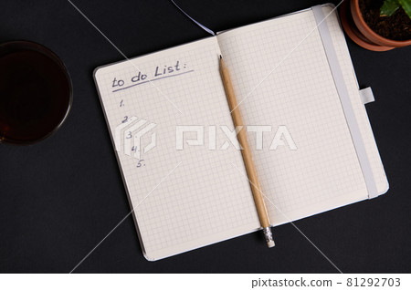 Wooden pencil on the opened agenda, organizer with list to do on blank white sheets, cup of coffee and potted succulent, on black background with copy space 81292703