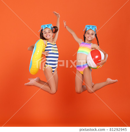 Two funny little sisters in swimsuits and goggles jumping up in air with inflatable swimming ring and ball Two funny little sisters in swimsuits and goggles jumping up in air with inflatable swimming ring and ball 81292945