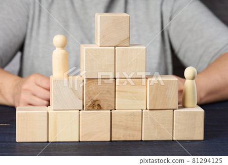 pyramids from wooden cubes and figurines of men on the table. The concept of achieving goals, moving up the career ladder. Detection of single-minded personality pyramids from wooden cubes and figurines of men on the table. The concept of achieving goals, moving up the career ladder. Detection of single-minded personality 81294125