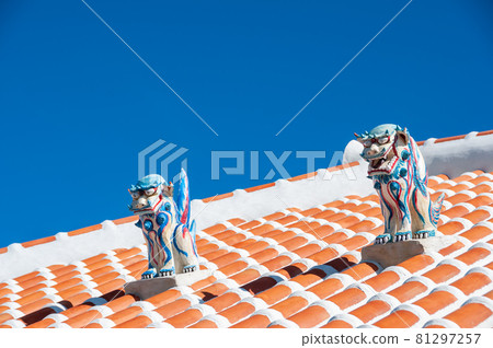 Amazing two highly colored Shisa statues, male and female, used as protection, on top of the red roof, blue sky. 81297257