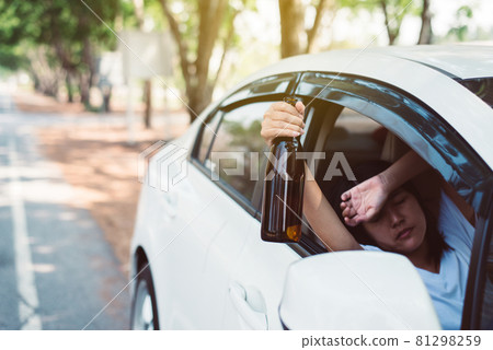 Drunk asian women drinking alcohol while driving car on road,Woman drive her car with a bottle of beer,Dangerous driving concept 81298259