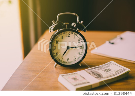 Clock and money US dollar banknote or bill on a working table,Saving money and management concept Clock and money US dollar banknote or bill on a working table,Saving money and management concept 81298444