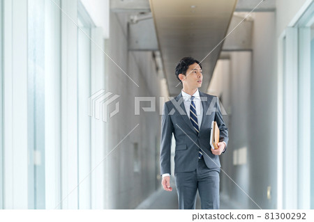 A young businessman in a suit walking in the office corridor A young businessman in a suit walking in the office corridor 81300292