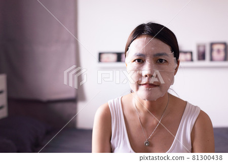 Asian woman applying moisturizing mask on her face skin at home 81300438