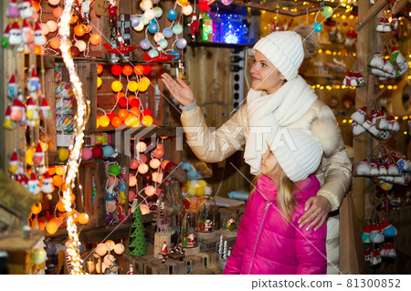 Cheerful little girl with mom choosing Christmas fairy lights at the street market 81300852