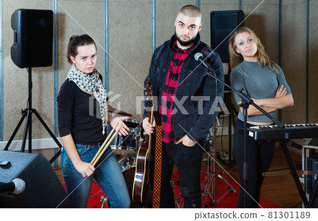 Three bandmates posing together with musical instruments in rehearsal room Three bandmates posing together with musical instruments in rehearsal room 81301189