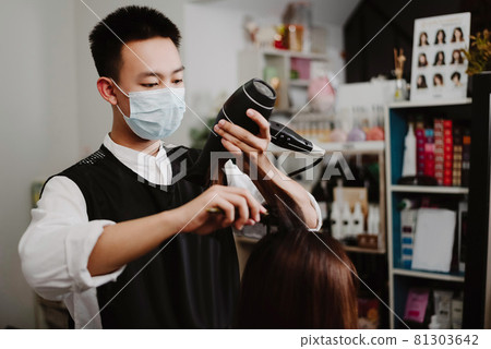 Hair salon concept a male hairstylist using a comb to grab a lock of hair and using hair dryer for drying and straightening 81303642