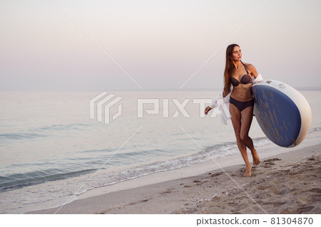 Young woman is carrying paddle board at the beach Young woman is carrying paddle board at the beach 81304870