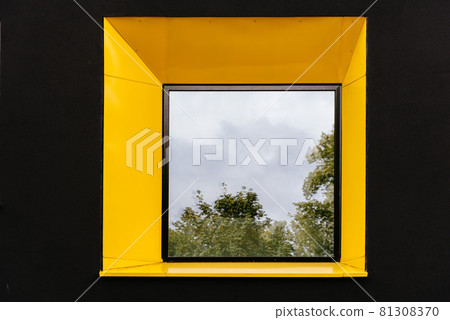 Yellow window on black facade with reflection of green tree on. Yellow window on black facade with reflection of green tree on. 81308370