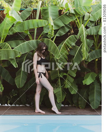 Young woman in a black bikini stands next to the pool. Hotel in the jungle. Summer in the tropics. Happy holiday Young woman in a black bikini stands next to the pool. Hotel in the jungle. Summer in the tropics. Happy holiday 81309086