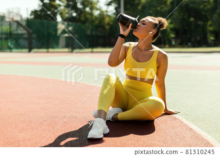 Portrait of sporty black woman in yellow sportswear drinking water Portrait of sporty black woman in yellow sportswear drinking water 81310245