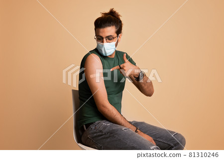Arab guy in face mask pointing at plaster on shoulder Arab guy in face mask pointing at plaster on shoulder 81310246