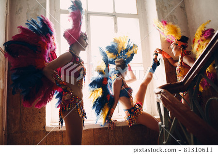 Woman in brazilian samba carnival costume with colorful feathers plumage relax in old entrance with big window 81310611