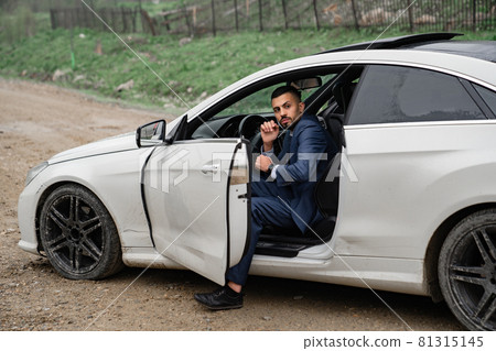 attractive man in business suit sits behind wheel of car with door open. 81315145
