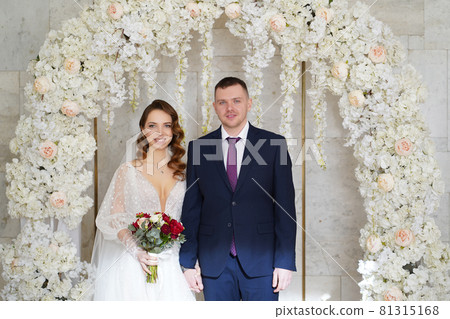 beautiful and happy bride and groom in an arch of flowers at wedding ceremony beautiful and happy bride and groom in an arch of flowers at wedding ceremony 81315168