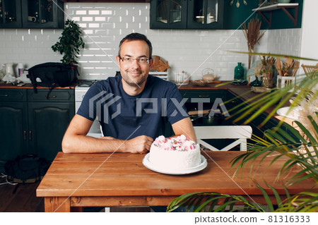 Man sit in home kitchen with cake on table 81316333
