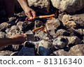 Human hands holding a sausage on a skewer and roasting it over a fire outdoor 81316340