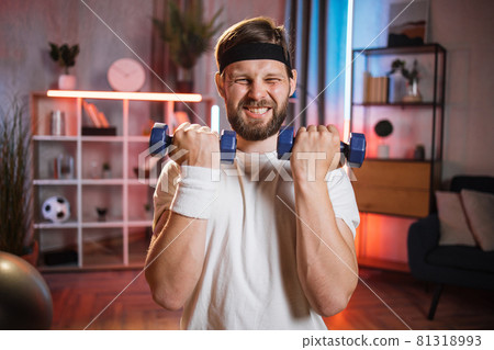 Man lifting dumbbells during evening time at home 81318993