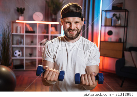 Man with effort face training arms using dumbbells at home 81318995