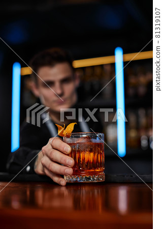 Barman holding out glass with alcoholic cocktail Barman holding out glass with alcoholic cocktail 81319107