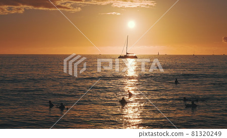 Amazing colors of a tropical sunset. Silhouettes of sailing boats floating on the ocean horizon. Surfers ride the waves. Oahu, summer vacation in Hawaii. Slow motion. 81320249