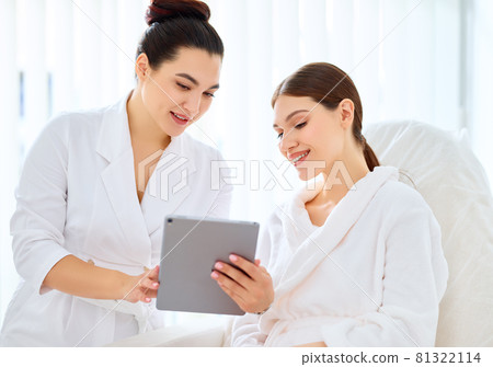 Cosmetologist and woman using tablet in clinic 81322114