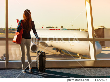 Travel during coronavirus pandemic tourist with luggage watching sunset at airport window. Unrecognizable woman waiting in lounge at boarding gate before departure. Travel lifestyle Travel during coronavirus pandemic tourist with luggage watching sunset at airport window. Unrecognizable woman waiting in lounge at boarding gate before departure. Travel lifestyle 81322824
