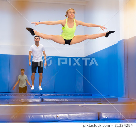 Woman practicing side split on trampoline Woman practicing side split on trampoline 81324294