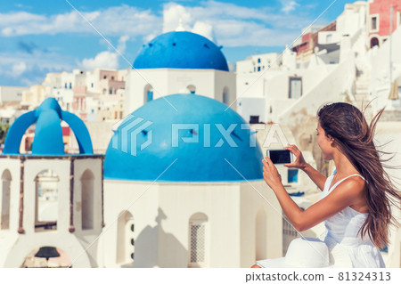 Travel tourist taking phone picture of Santorini Blue dome church, touristic attraction in Europe, European vacation banner. Woman taking smartphone photo of famous destination. Travel tourist taking phone picture of Santorini Blue dome church, touristic attraction in Europe, European vacation banner. Woman taking smartphone photo of famous destination. 81324313