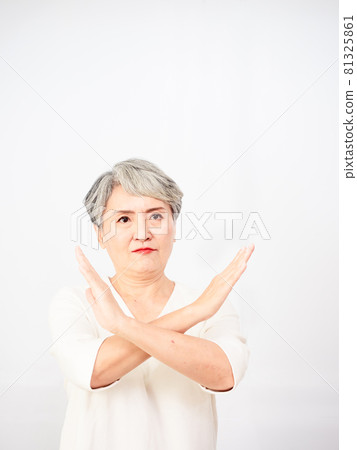 A mature, beautiful, gray-haired woman in a leisurely outfit, with hands and palms crossed. A warning expression on a white background with a neutral and peaceful expression. 81325861